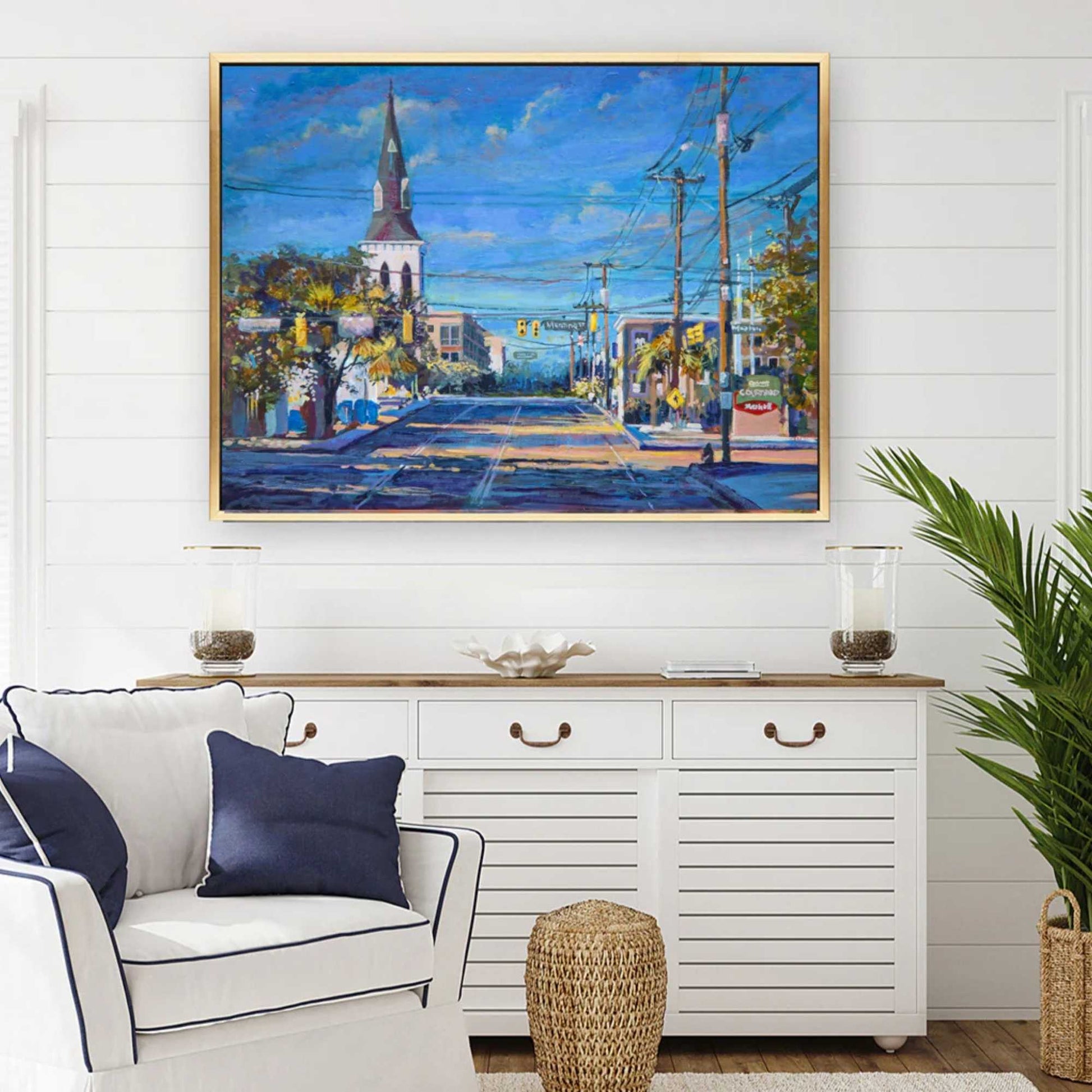 Living room with a painting of a Charleston by Patrick Reid O'Brien on the wall, white sofa, and decorative items.