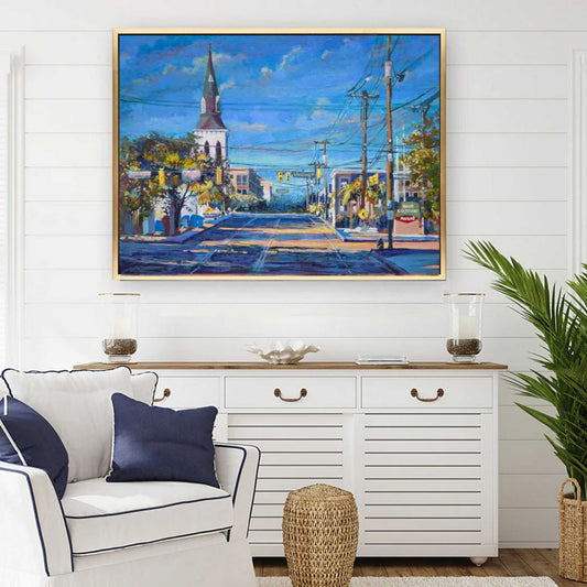 Living room with a painting of a Charleston by Patrick Reid O'Brien on the wall, white sofa, and decorative items.
