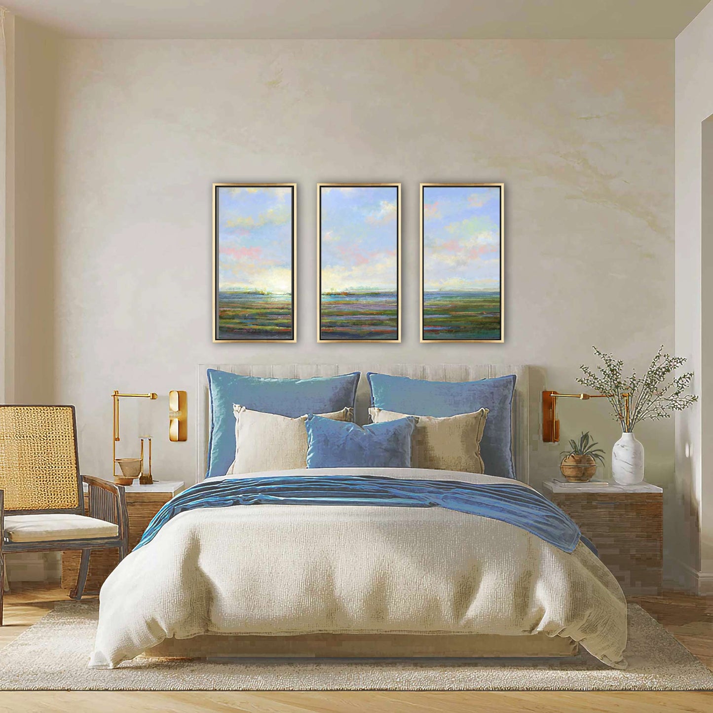 Bedroom with a bed featuring blue and beige bedding, three framed artworks above the bed, and a side table with a lamp.