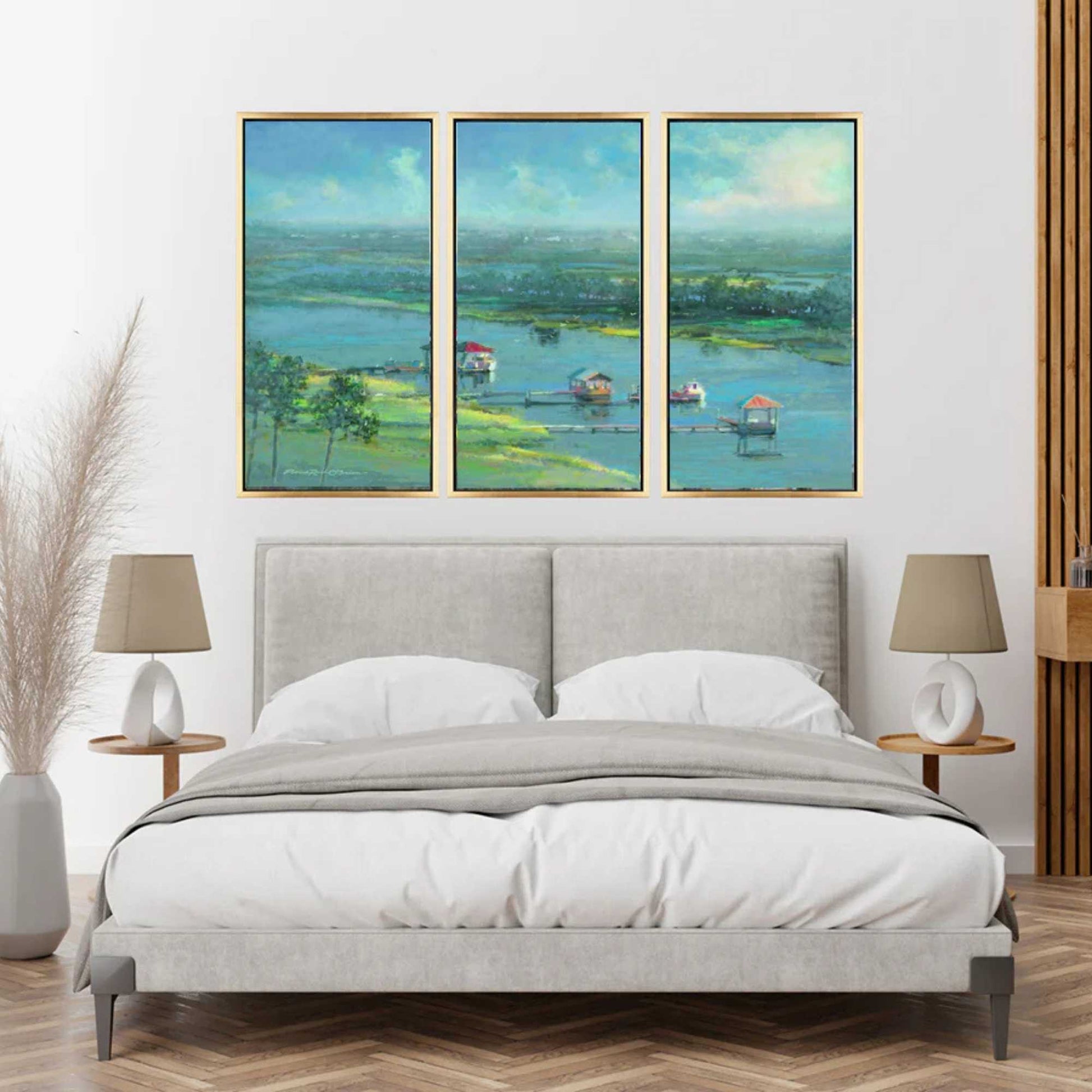 Bedroom with a gray upholstered bed, two lamps, and one three panel triptych by Patrick Reid O'Brien framed landscape painting on the wall. The triptych reads like windows opening up the room.