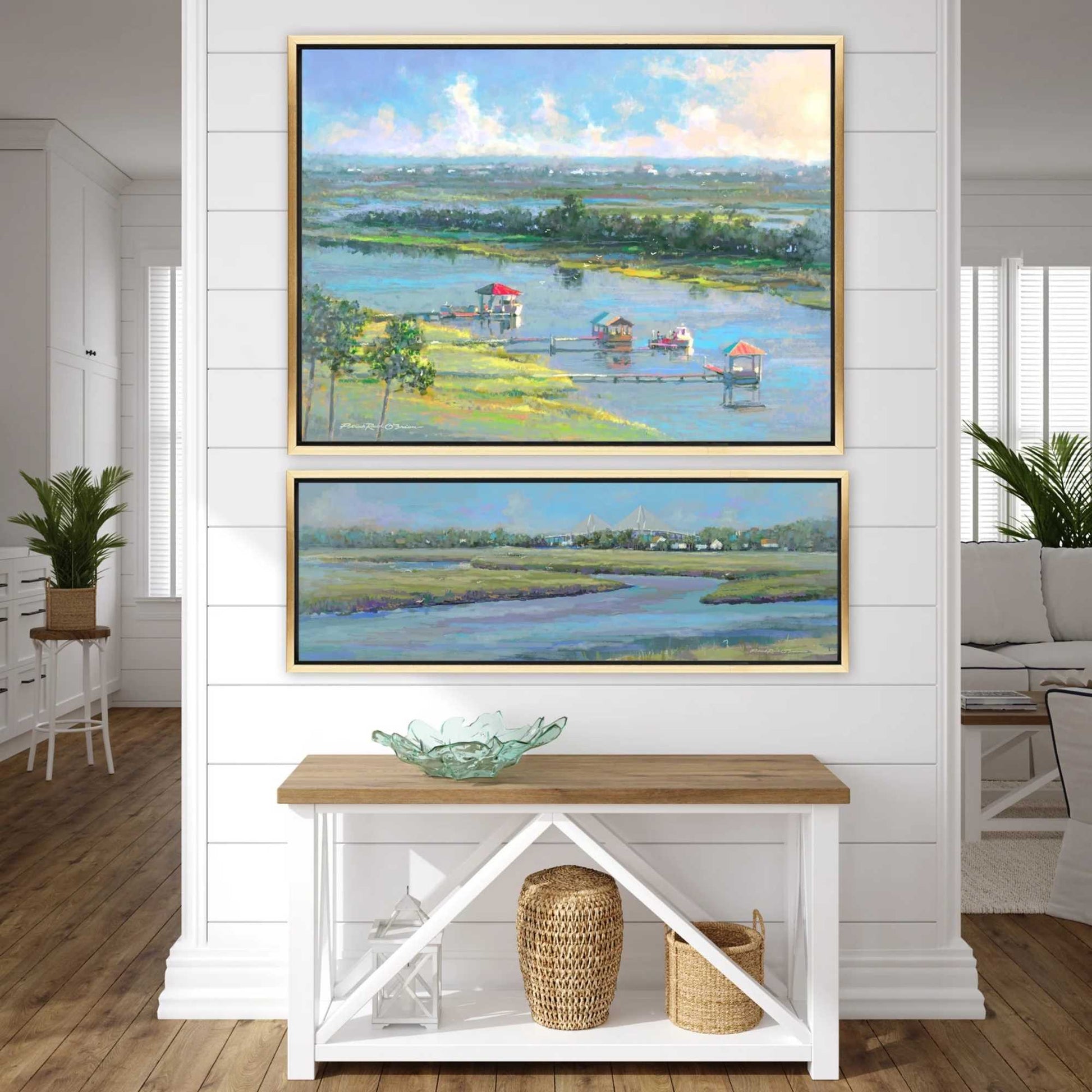 Two framed paintings of a landscape scene hanging on a white wall above a wooden console table.