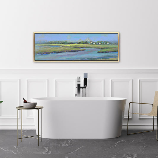 Modern bathroom with a freestanding bathtub, side table, and chair, featuring a large framed landscape painting on the wall.