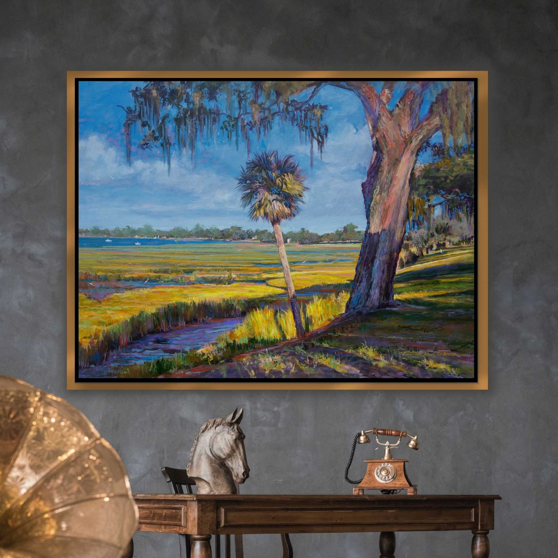Framed painting of an impressionist marsh landscape by Patrick Reid O'Brien with trees and fields on a gray wall above a classical antique wooden table.