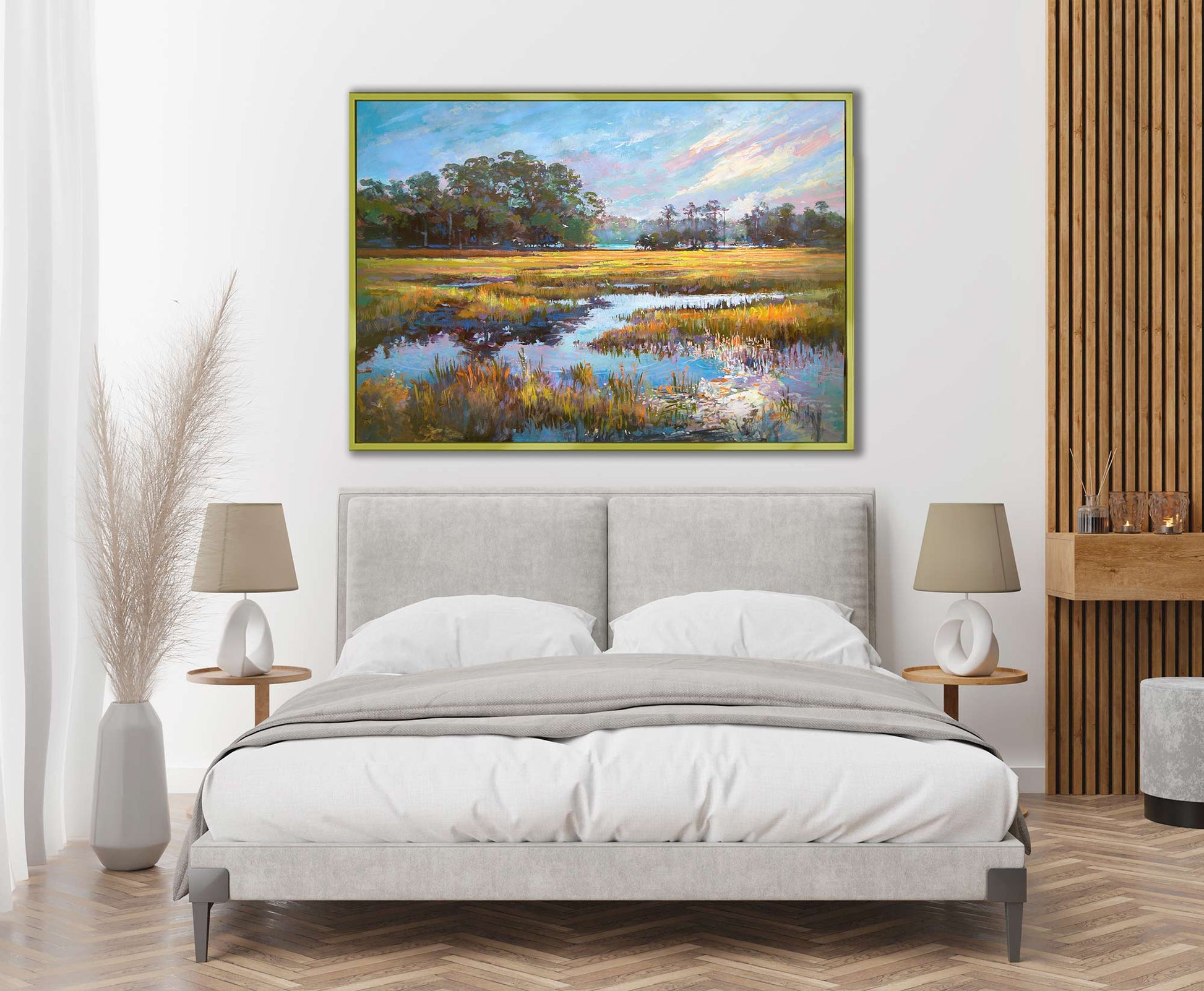 This image features a beautifully vibrant painting titled "Closer to my Home," by Patrick Reid O'Brien hanging elegantly above a bed in a stylishly decorated room. The artwork captures the serene beauty of a marshy landscape with vivid blue skies and lush greenery, reflecting a sense of peace and tranquility.